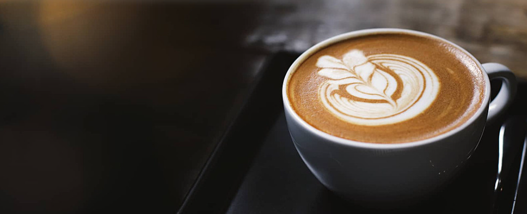 Café con arte latte en taza de color blanco sobre bandeja negra
