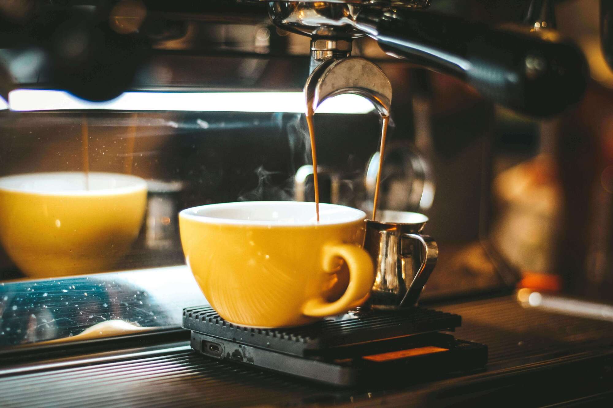 Máquina de café expreso sirviendo café en una taza amarilla con interior blanco y en una jarra metálica