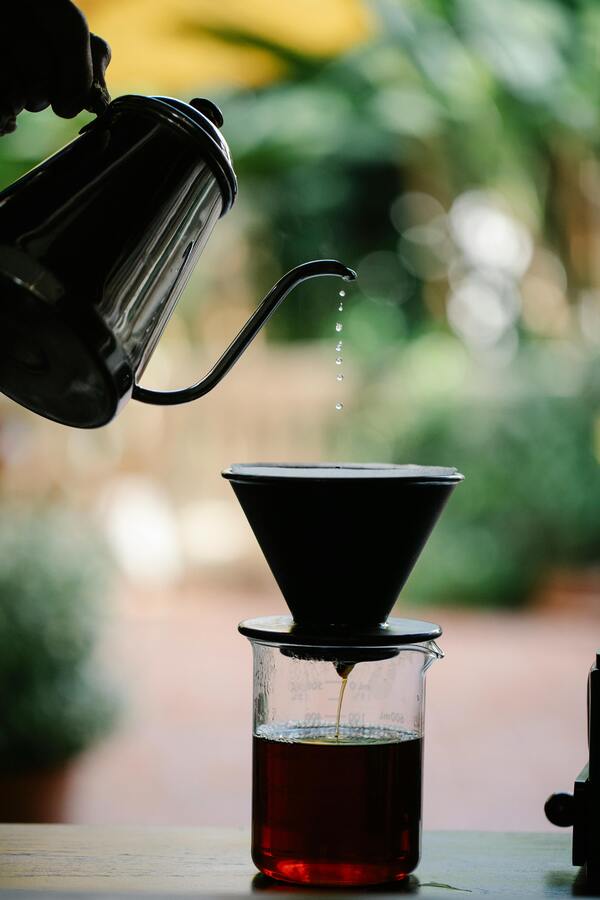 Jarra sirviendo agua sobre un filtro cónico que gotea café dentro de un vaso de vidrio